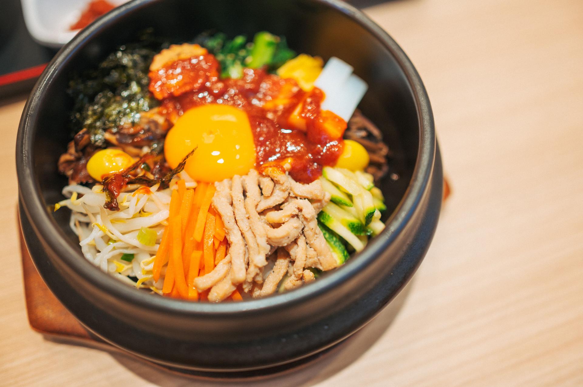 a deliciously arranged bowl of bibimbap, featuring a mix of fresh vegetables, savory meat, and a raw egg yolk. the vibrant presentation celebrates the harmony of flavors and textures in korean cuisine.